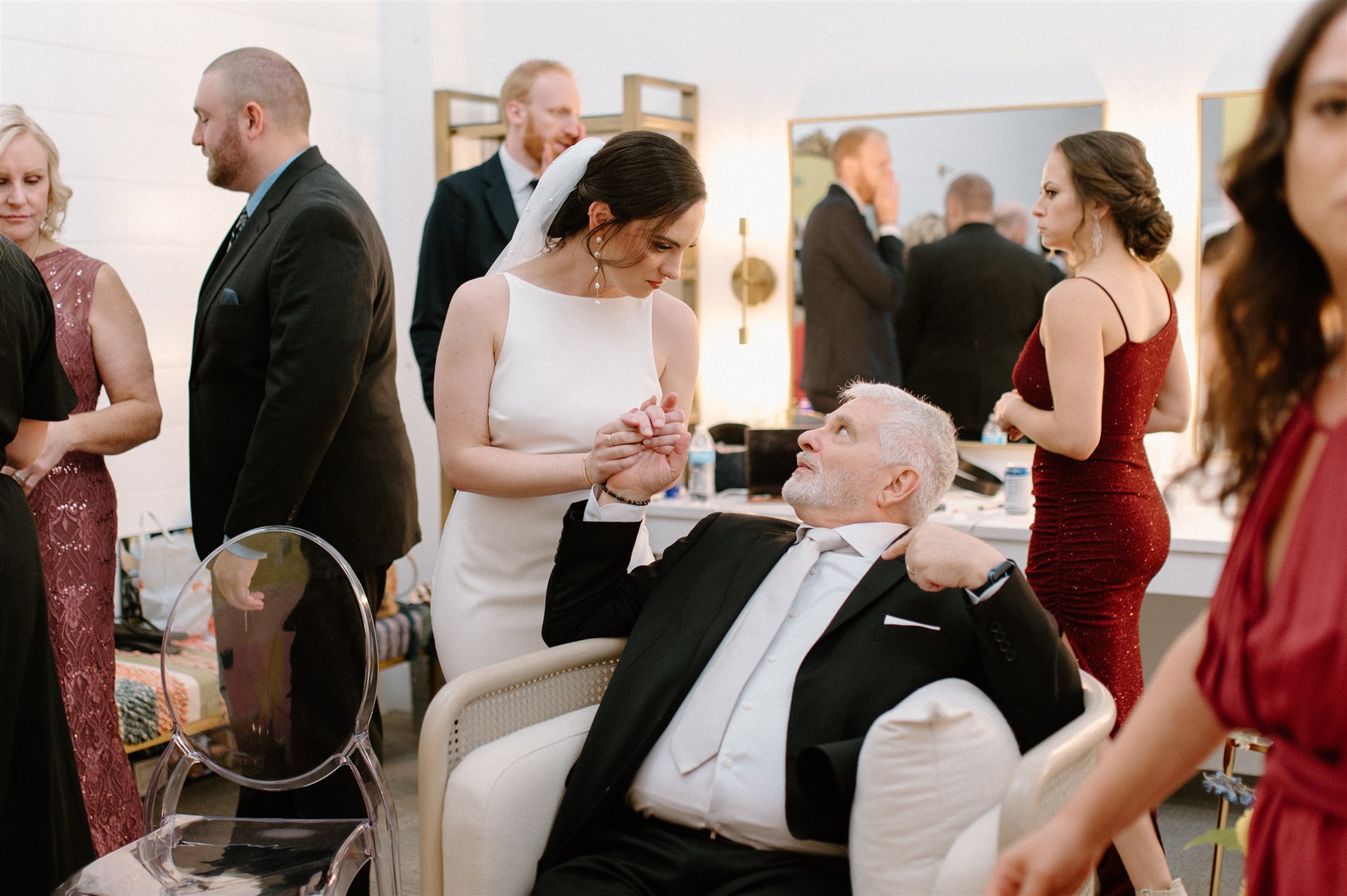 Bride and dad hold hands and lock eyes while others walk around them in a room