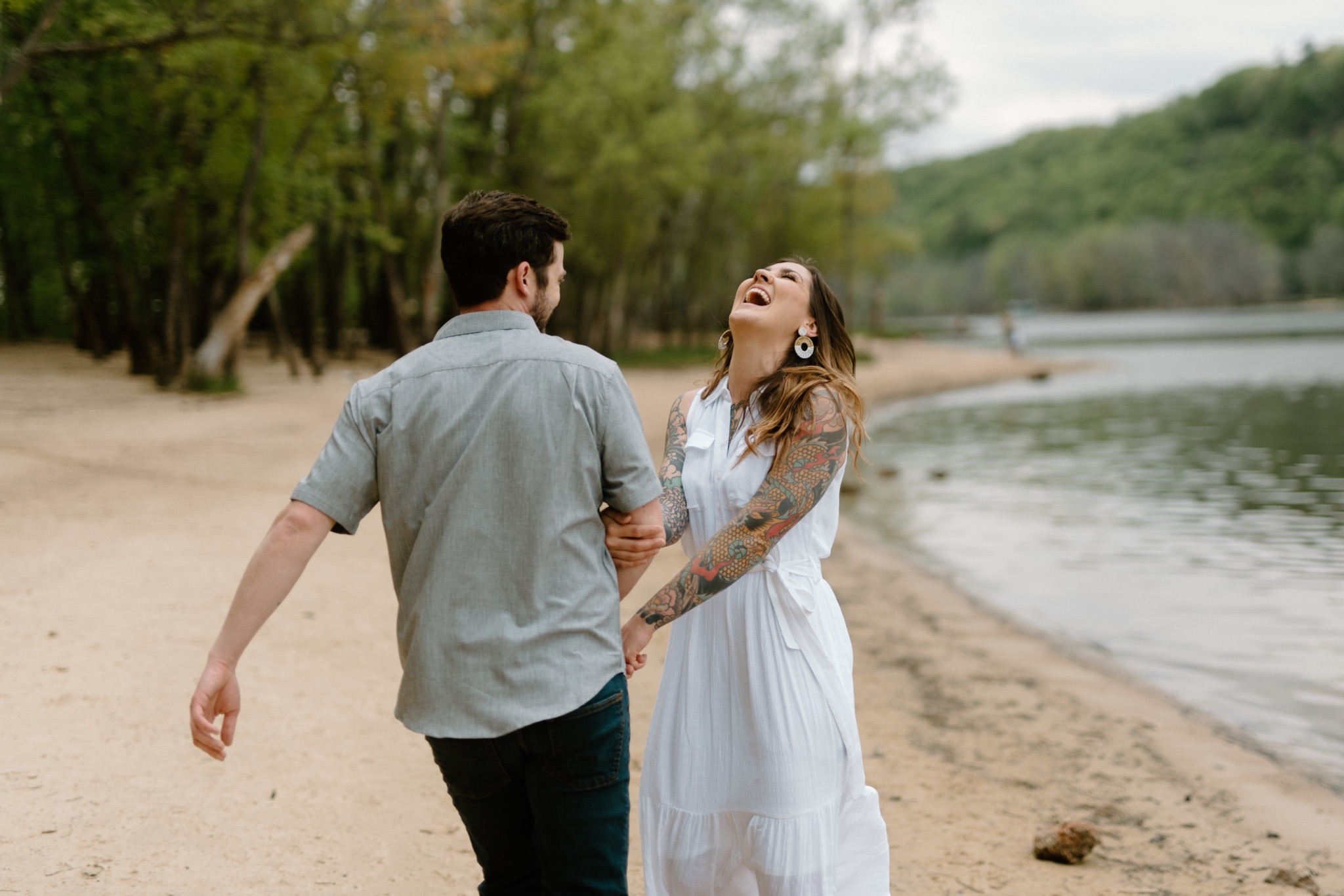man and woman laughing and walking on sand