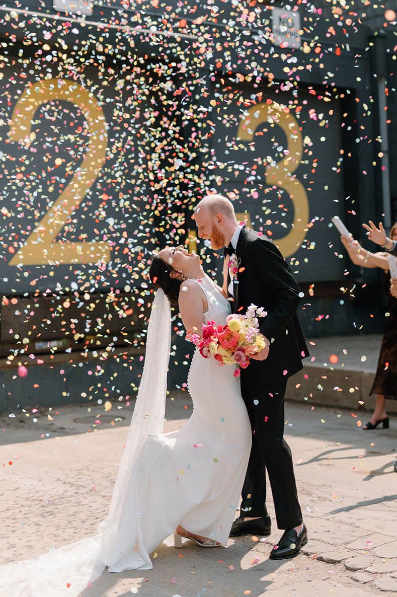 Bride and groom celebrate under rainbow confetti popping in the sky
