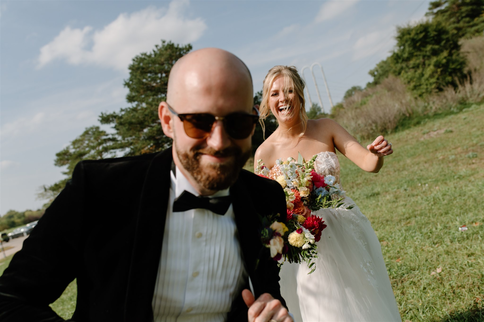 Bride and groom smile candidly directly into camera at an angle on a sunny day